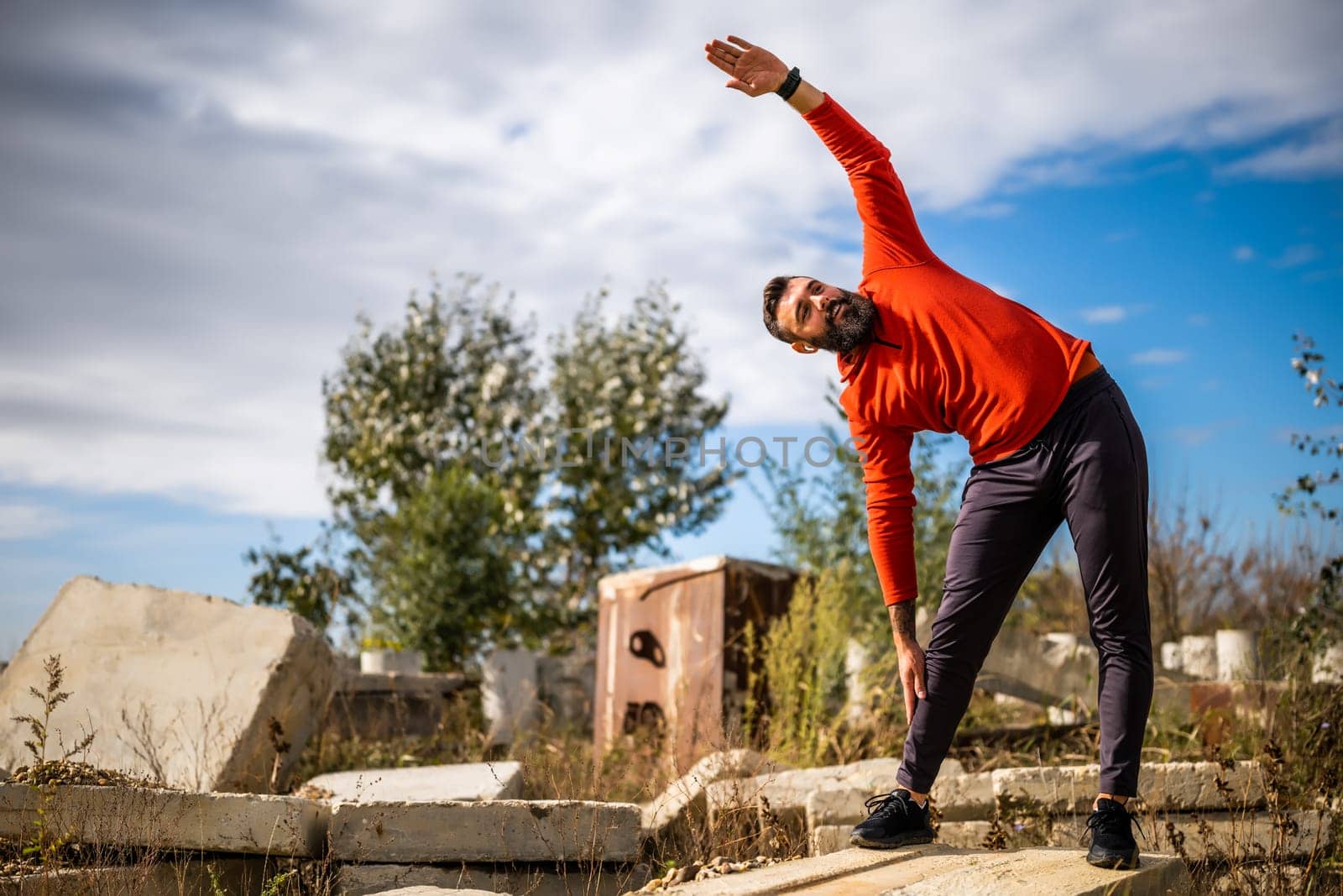 Adult man is exercising outdoor on sunny day. He is stretching his body.