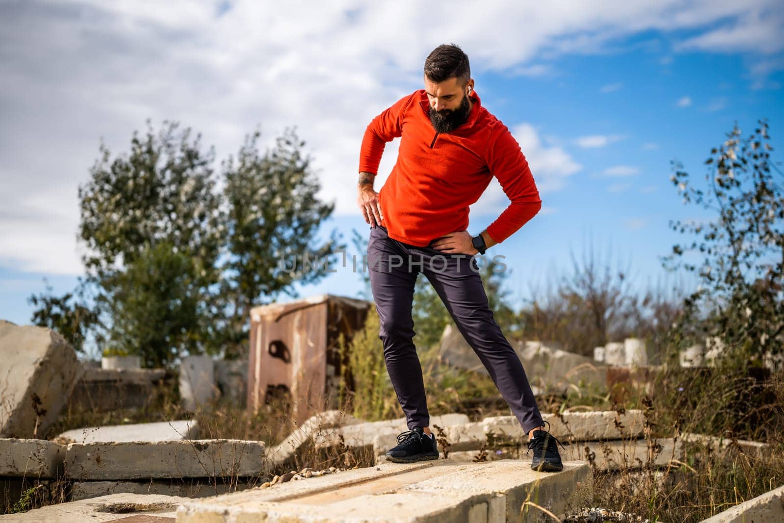 Adult man is exercising outdoor on sunny day. He is stretching his body.