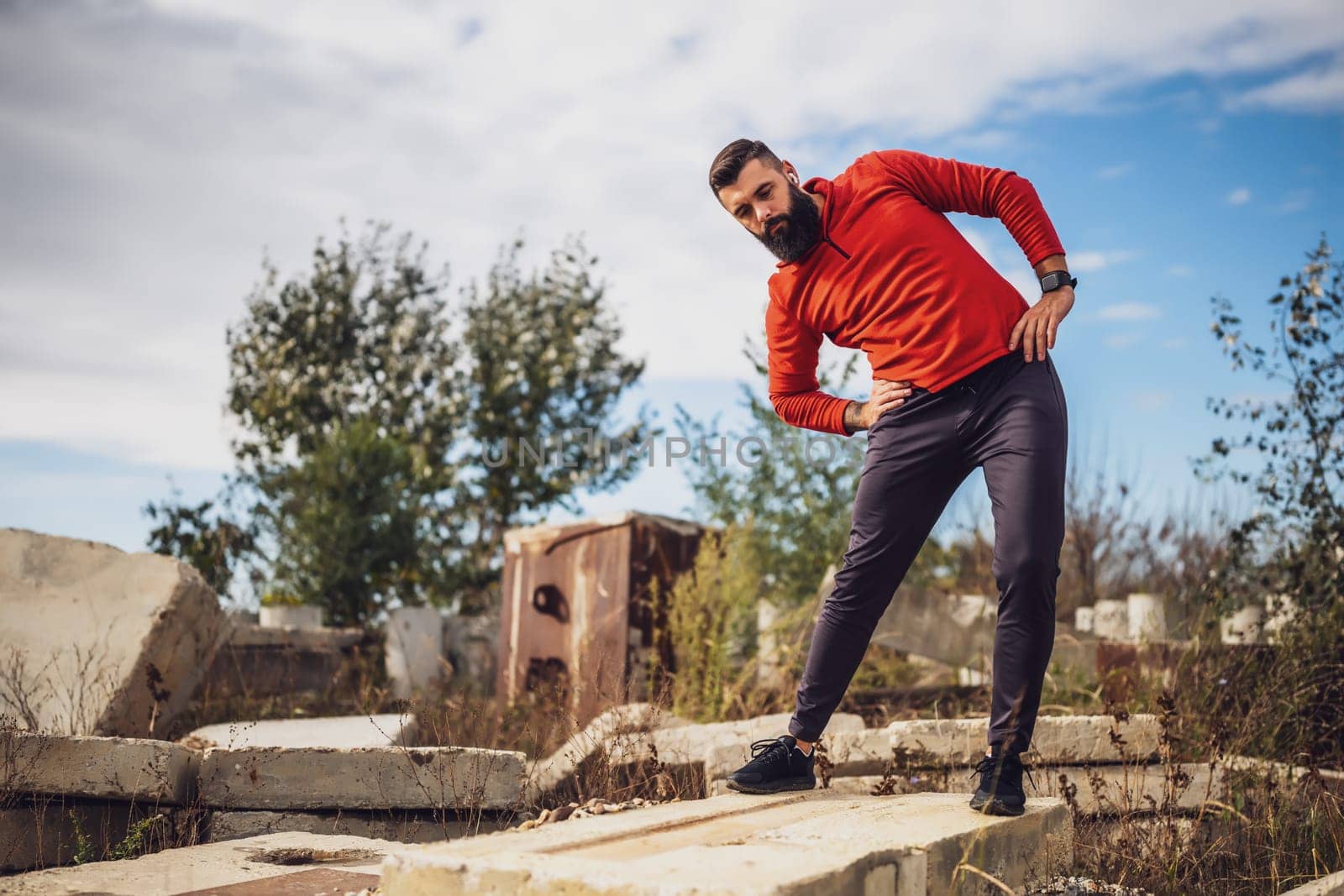 Adult man is exercising outdoor on sunny day. He is stretching his body.