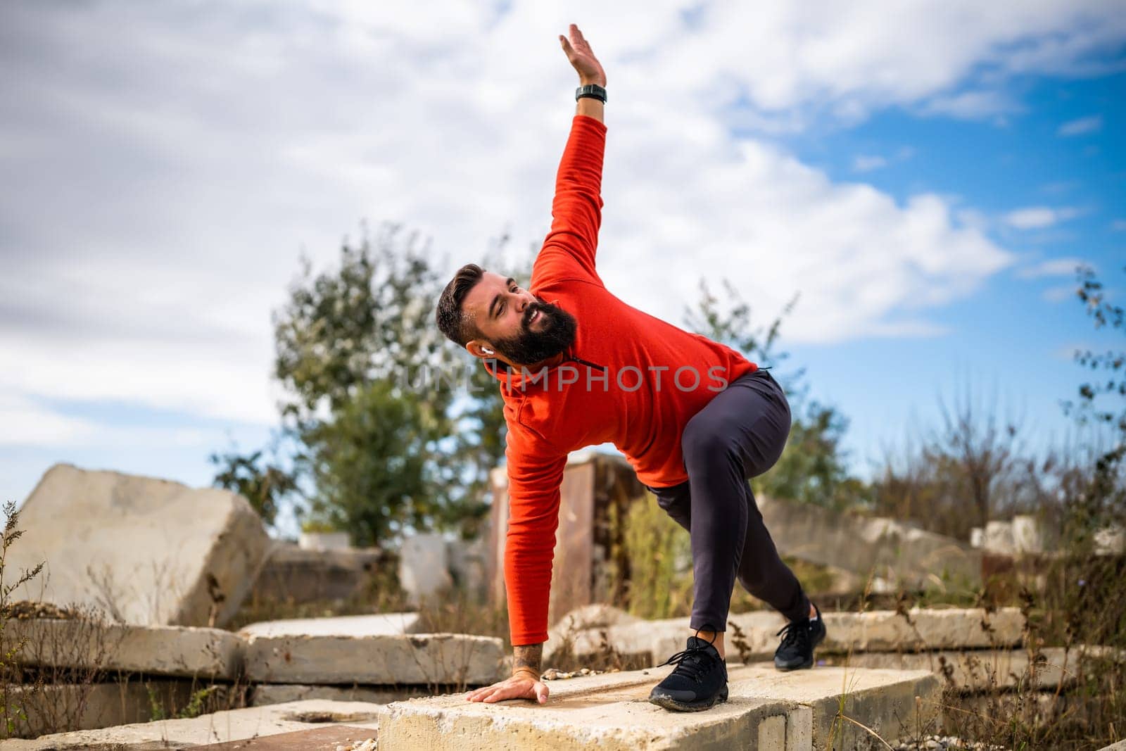 Adult man is exercising outdoor on sunny day. He is stretching his body.