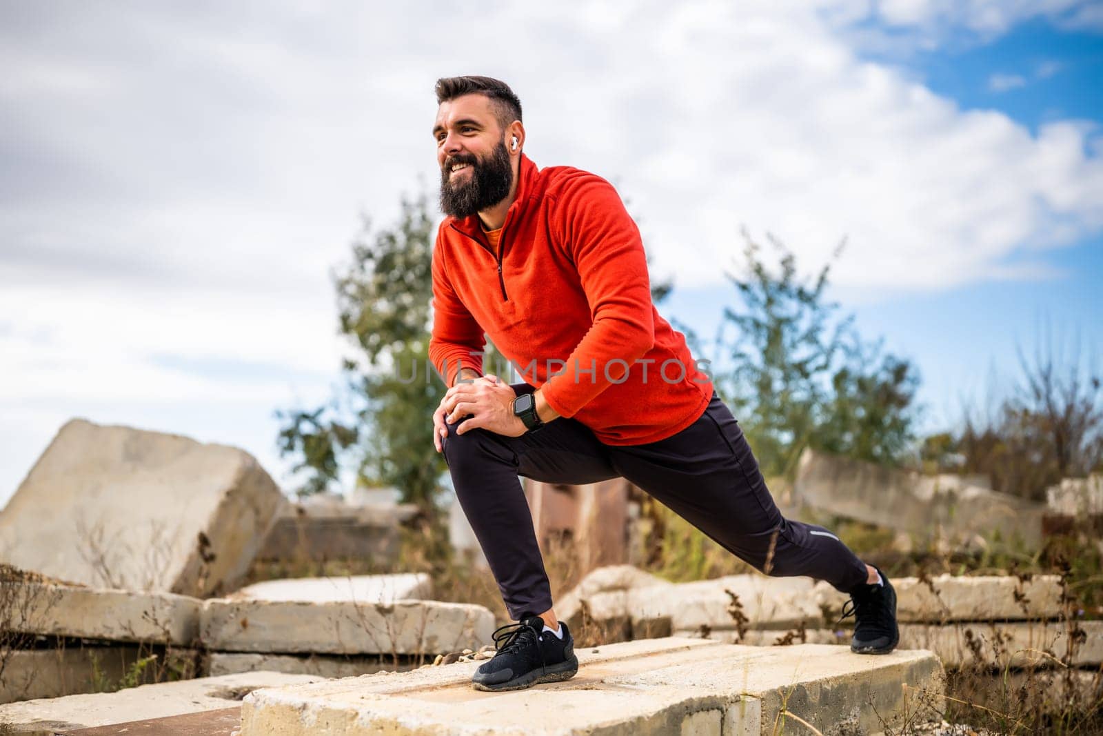 Adult man is exercising outdoor on sunny day. He is stretching his body.