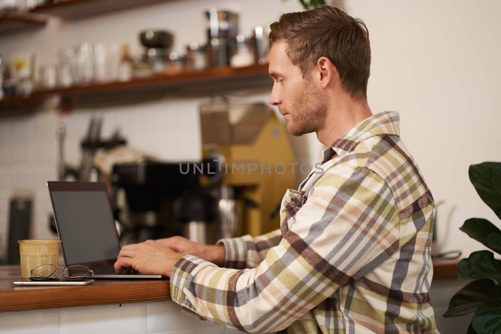 Portrait of young man, digital nomad working on project, using laptop in cafe, drinking coffee and typing, browsing on the internet.