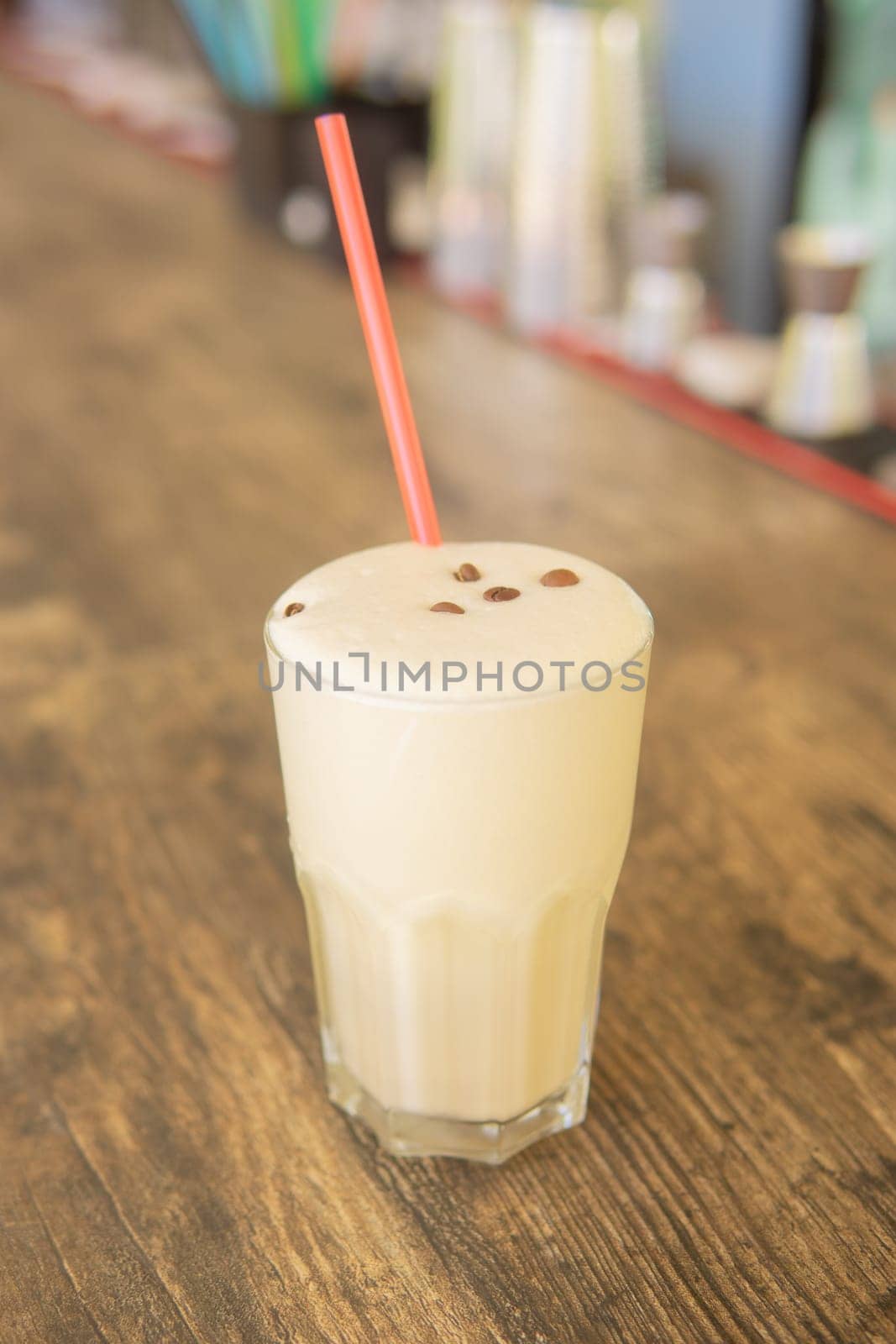 A cold coffee cocktail in a clear glass with a straw on a wooden bar counter.