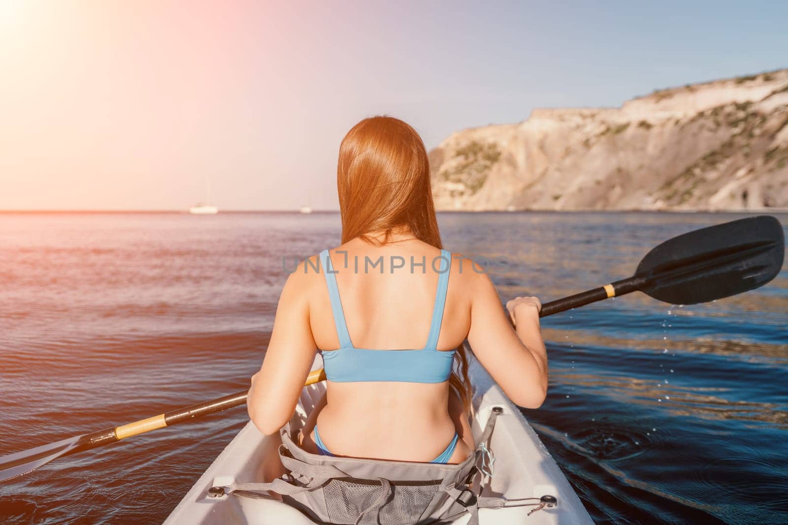 Woman in kayak back view. Happy young woman with long hair floating in transparent kayak on the crystal clear sea. Summer holiday vacation and cheerful female people relaxing having fun on the boat