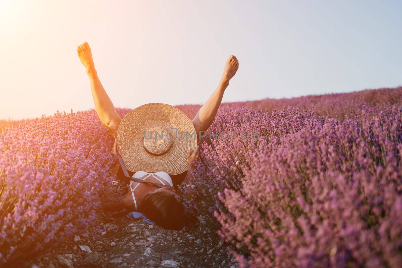 Woman lavender field. Happy carefree Woman legs stick out of the lavender bushes, warm sunset light. Bushes of lavender purple in blossom, aromatic flowers at lavender fields. by panophotograph