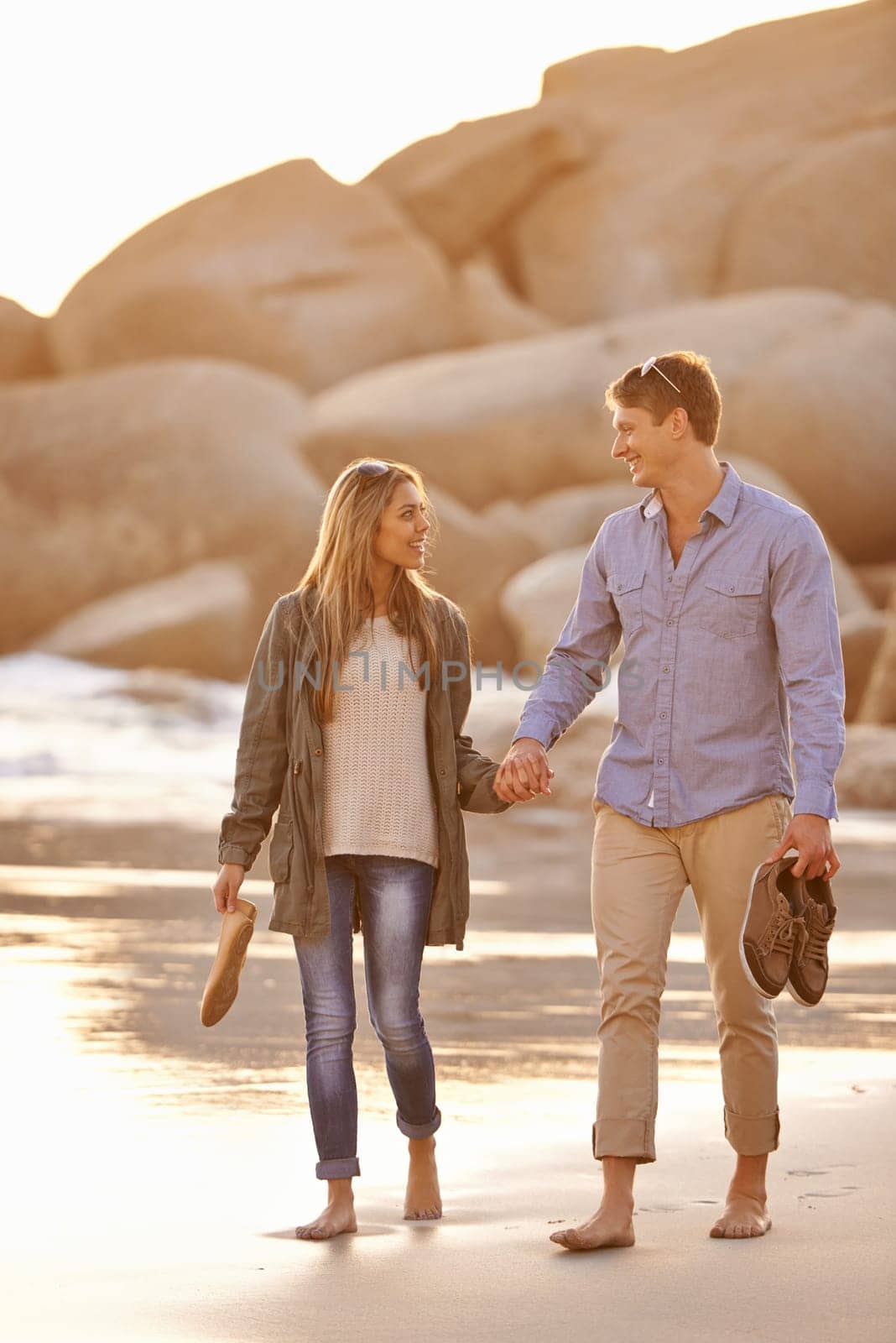 Love, holding hands and couple on walk with ocean, sunset and tropical holiday adventure, relax and bonding together. Rocks, man and woman on romantic date with beach, nature and travel on vacation by YuriArcurs