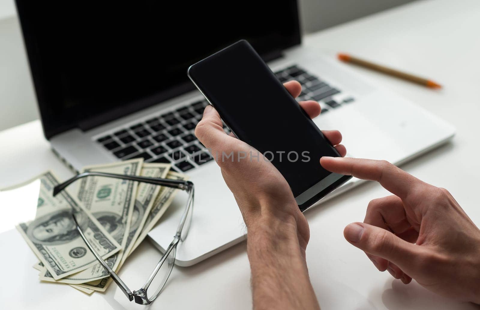 Mixed race man in glasses working with multiple electronic internet devices. Freelancer businessman has tablet and cellphone in hands and laptop on table with charts on screen. Multitasking theme. High quality photo