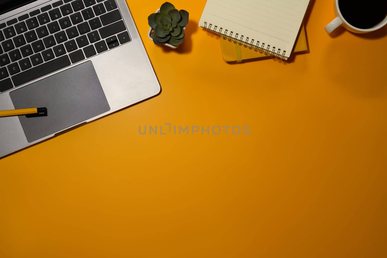 Top view laptop, cup of coffee, notepad and small potted plant on yellow background with copy space.
