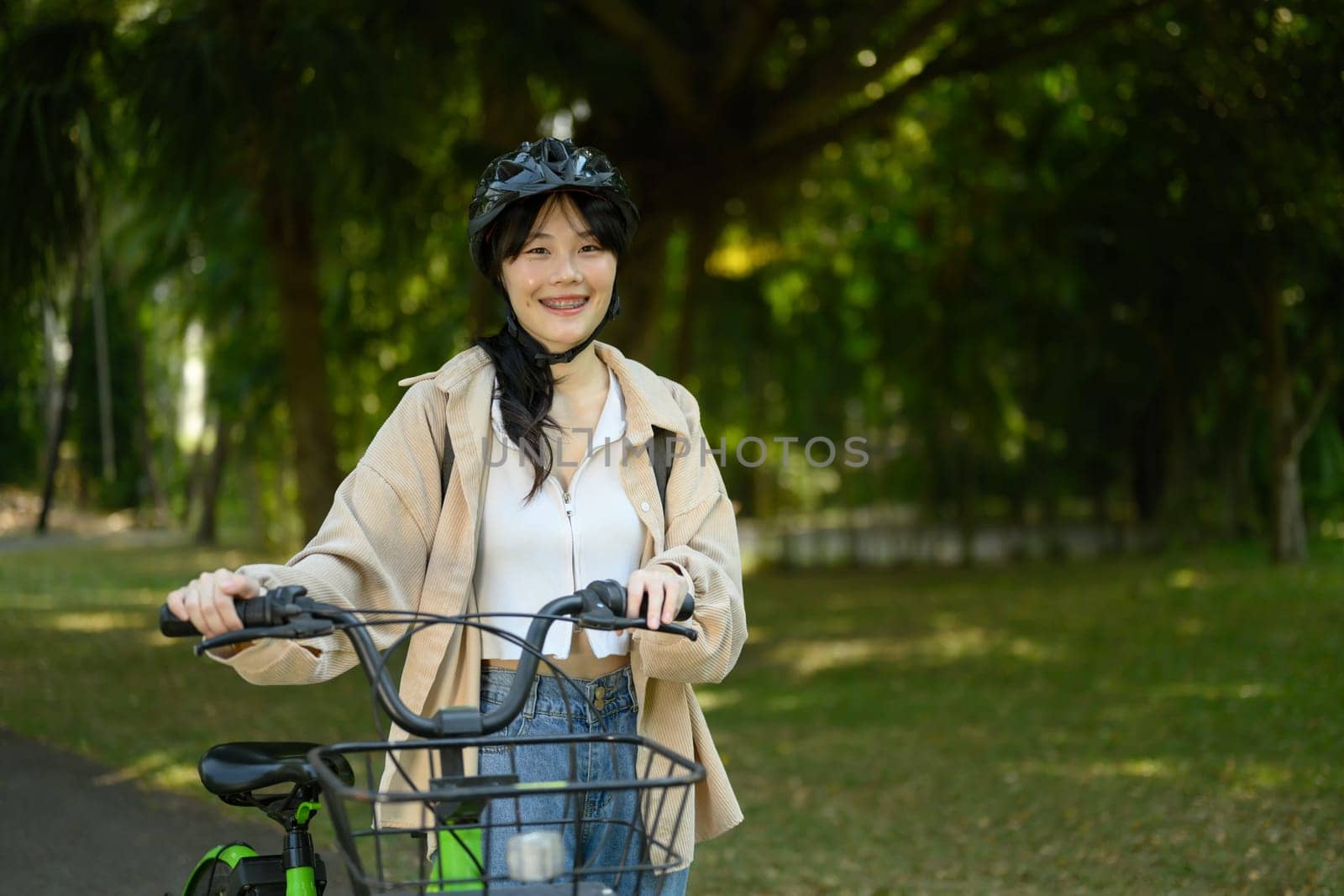 Smiling young woman in helmet walking with bicycle in city park on beautiful spring day.