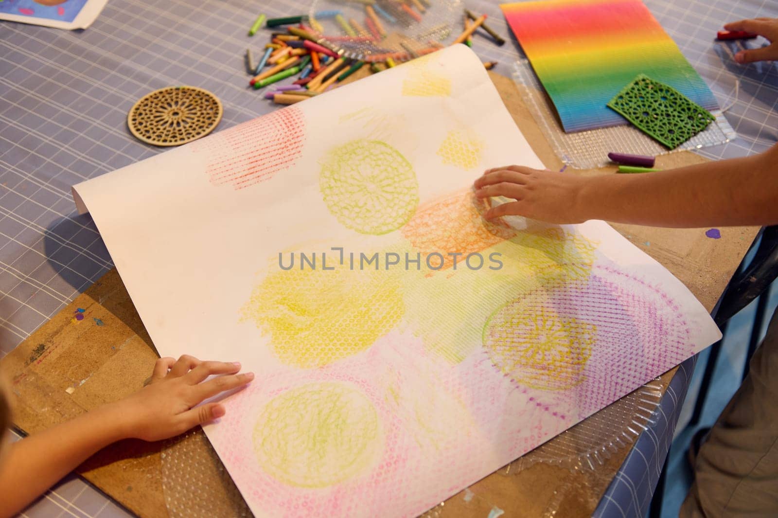 Close-up hands of children drawing with pastel color pencils on cardboard paper, learning painting during art class lesson in a creative workshop. People. Creative hobby for children. Education