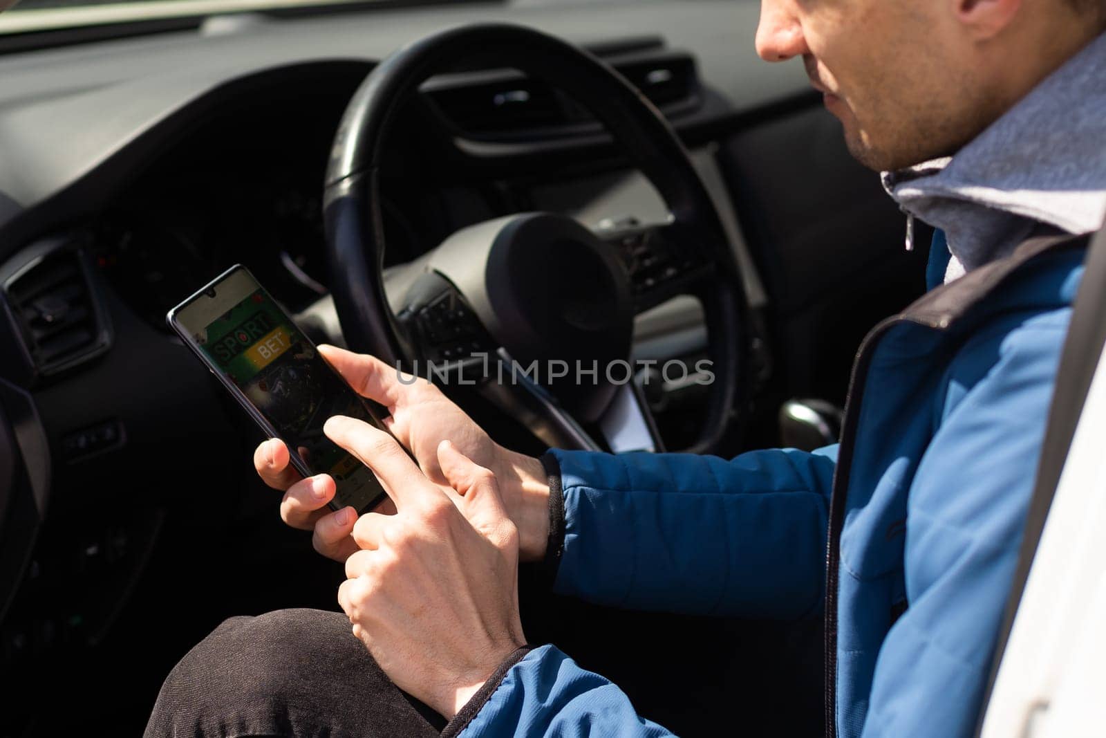 Close up cropped shot of man hand holding mobile phone with bookmaker;s website on its screen. Male gambler betting online using mobile application white sitting in a car