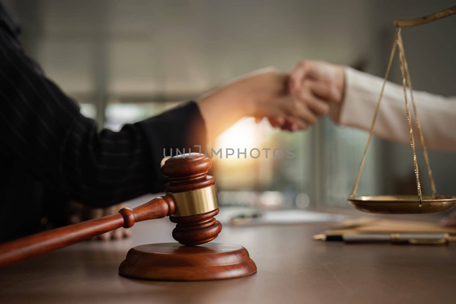 A lawyer and a businesswoman shake hands and reach an agreement on a cooperation contract document. In the lawyer's office and there is a hammer lying on the table. by wichayada