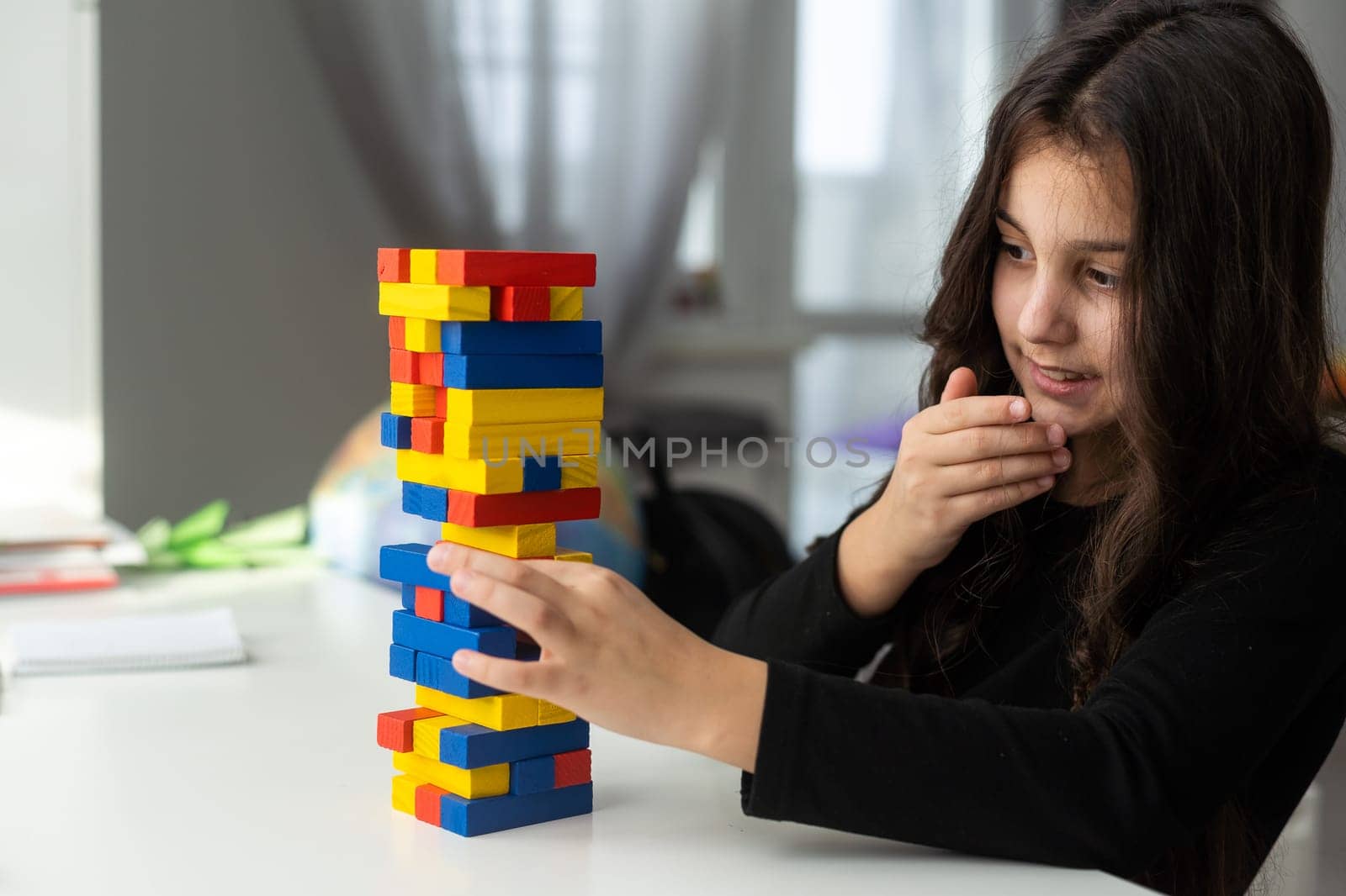 a little happy girl is playing the board game jenga at the table. Construction of a tower made of wooden cubes.