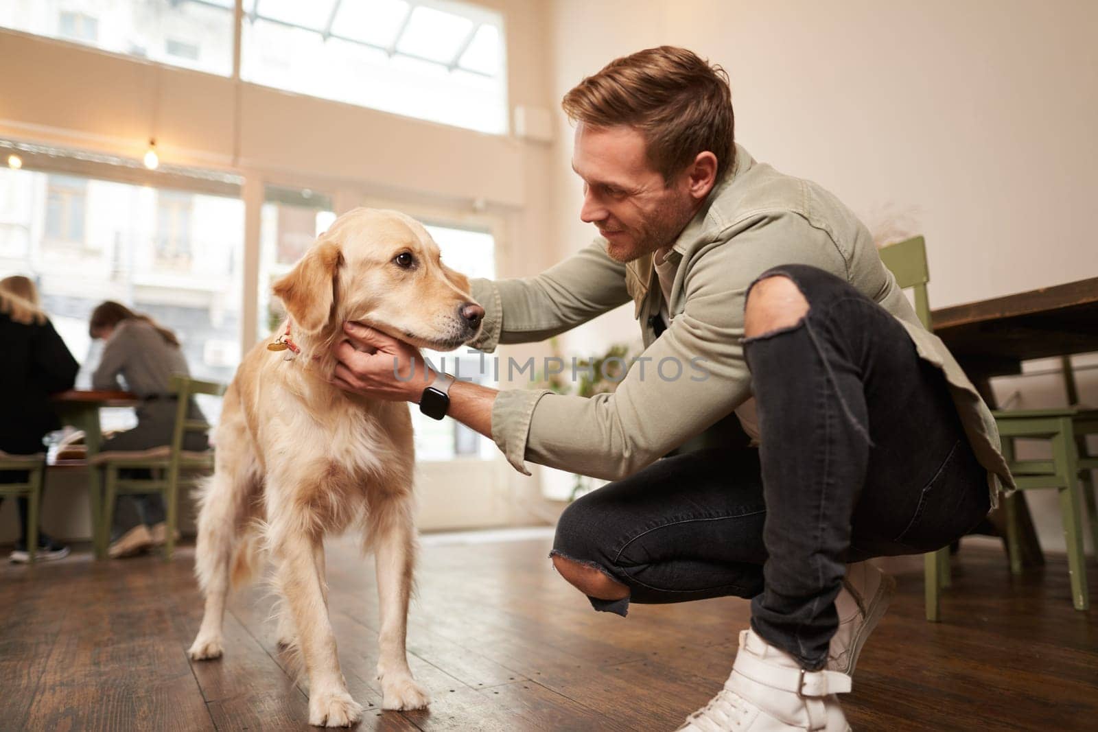 Close up portrait of handsome happy man petting his cute dog in a pet-friendly cafe. Coffee shop visitor with his golden retriever.