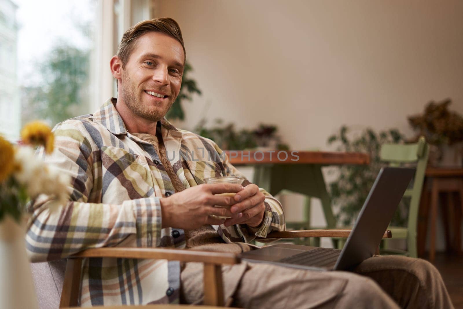 Handsome young professional, businessman sitting in cafe with glass of coffee and working on laptop, searching for inspiration outside of office workspace.