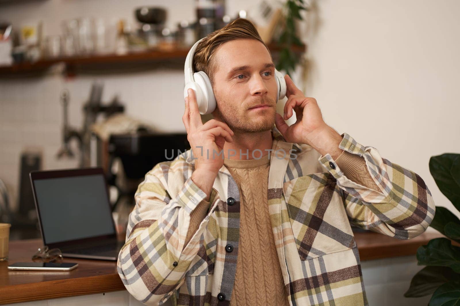 Portrait of handsome happy guy, freelancer working and listening to music in wireless headphones, dancing on his chair in cafe, enjoying favourite song in earphones by Benzoix