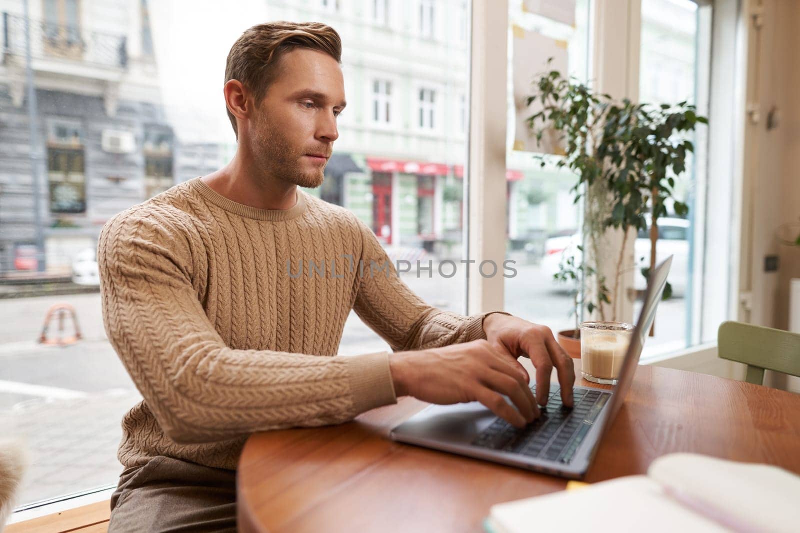 Serious looking cafe owner, handsome man working on laptop, visitor in coffee shop sending an email, typing on his keyboard.