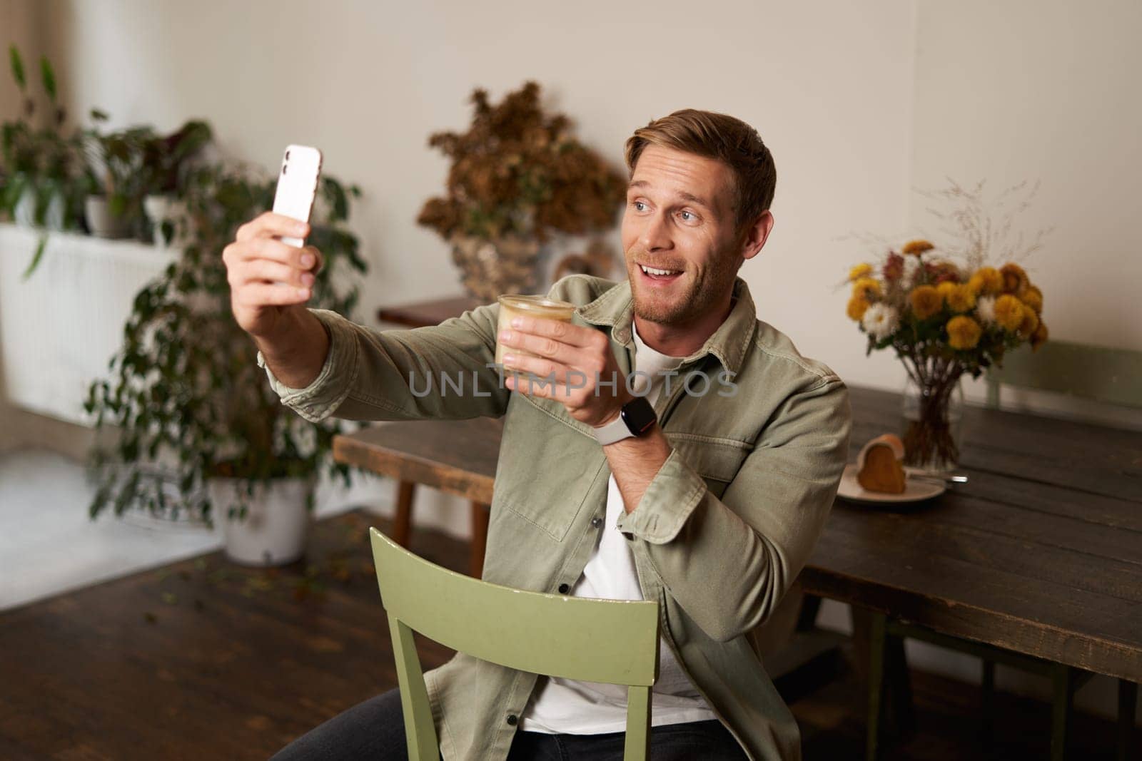 Portrait of handsome happy young man, taking selfie in cafe, posing with cup of coffee, video chats using smartphone app, talks to a friend. Lifestyle and leisure concept