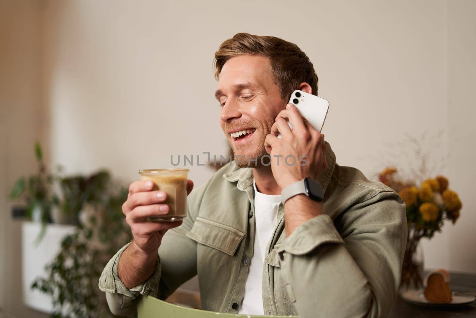 Portrait of young handsome man talking on the phone, drinks coffee and laughs. A guy sits in cafe having a nice, pleasant conversation over cup of cappuccino.