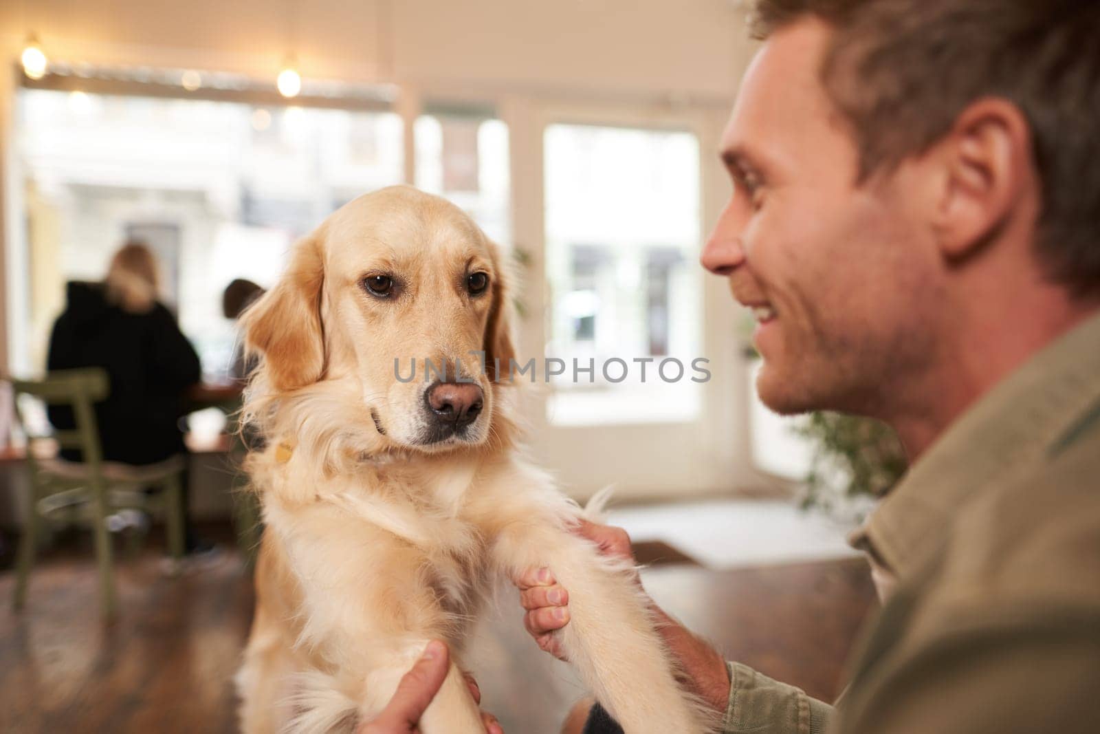 Close up portrait of young man with his pet in coffee shop. Dog owner playing with his pet, looking happy.