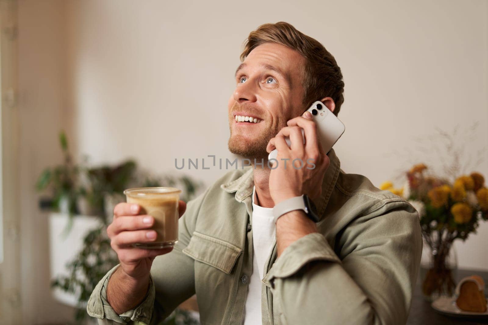 Portrait of handsome young man talking on the phone, sitting in cafe and drinking coffee, answering a call.