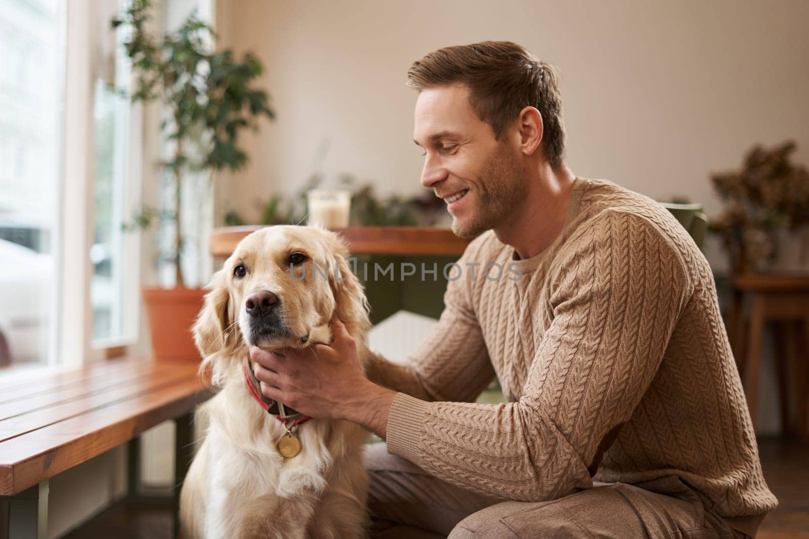 Dog friendly cafe and restaurants. Close up portrait of happy, handsome man pets his golden retriever inside the coworking space by Benzoix