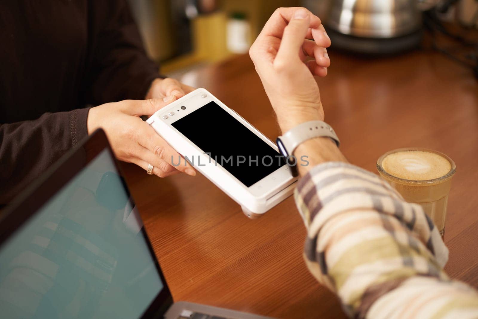 Man in cafe paying contactless using his digital watch on wrist, holding it close to the POS contactless terminal, working from coworking.