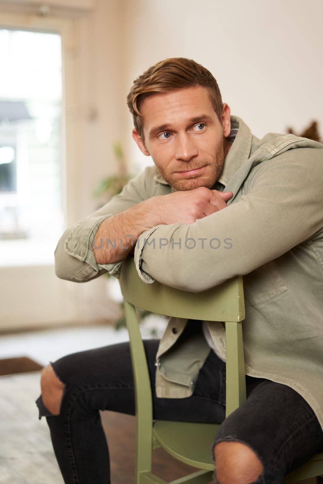 Vertical portrait of handsome masculine man, sitting on chair, looking aside, waiting for an order in coffee shop.