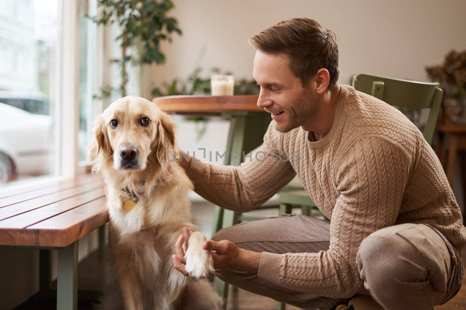 Portrait of young handsome man with his dog, sitting in cafe, golden retriever gives paw and looks at his owner.