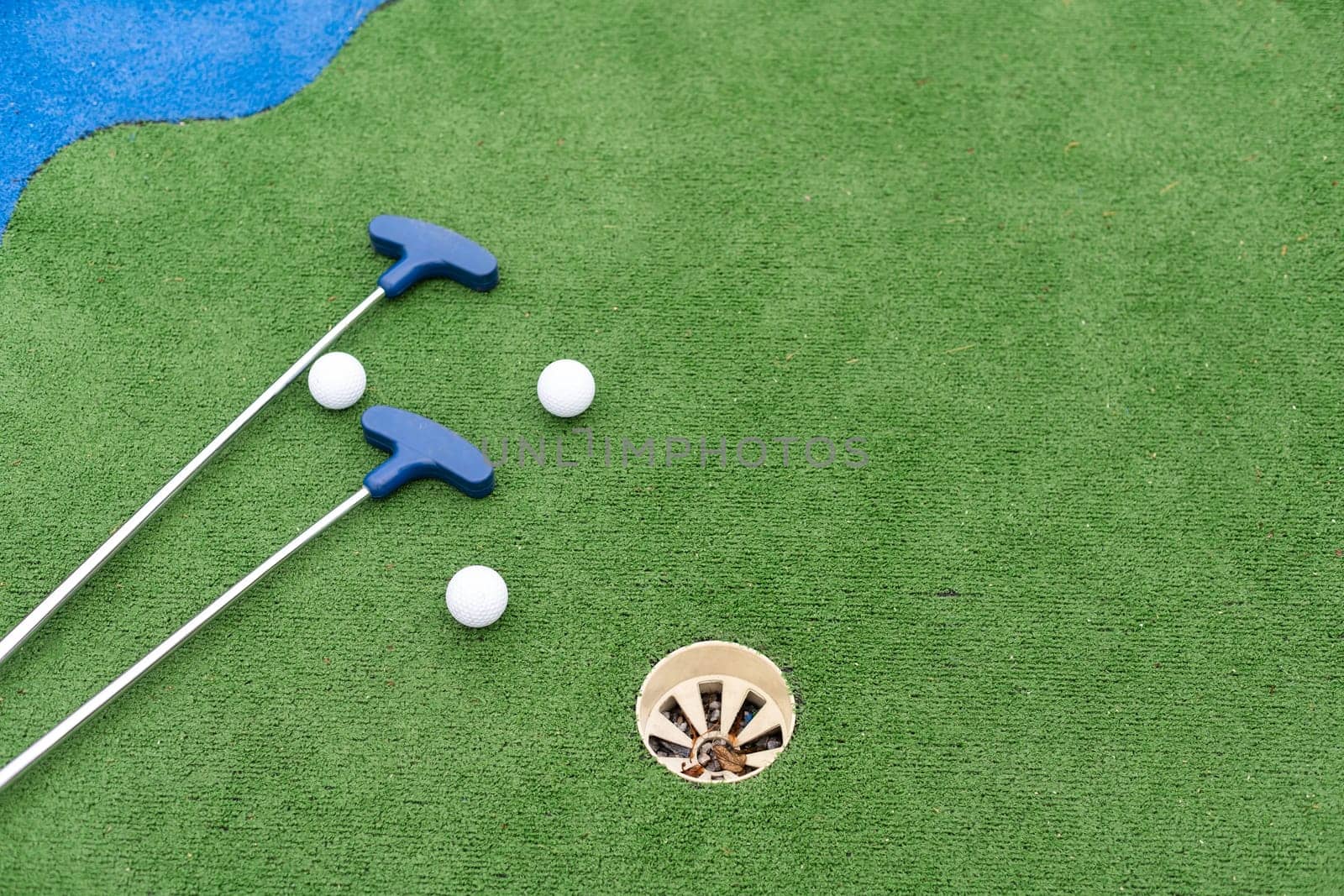 Mini-golf clubs and balls of different colors laid on artificial grass. High quality photo