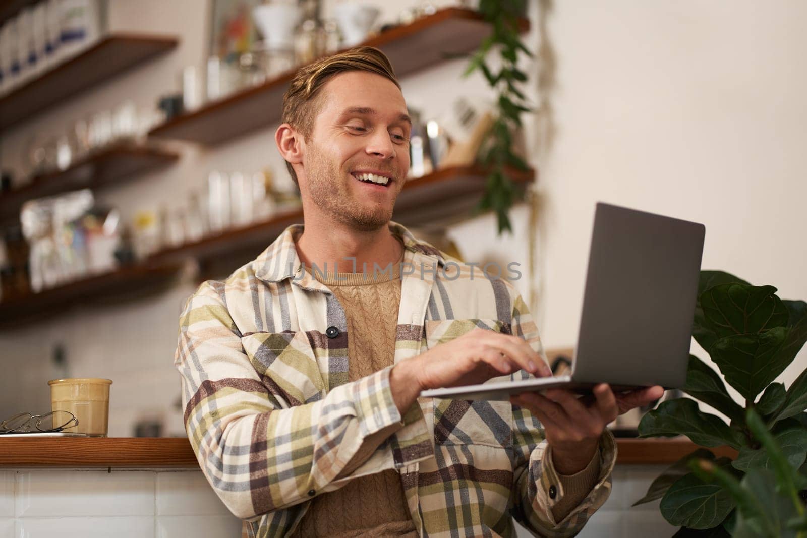 Image of young man in coffee shop, connects to video call, talking online, chats with friends via laptop and smiles by Benzoix