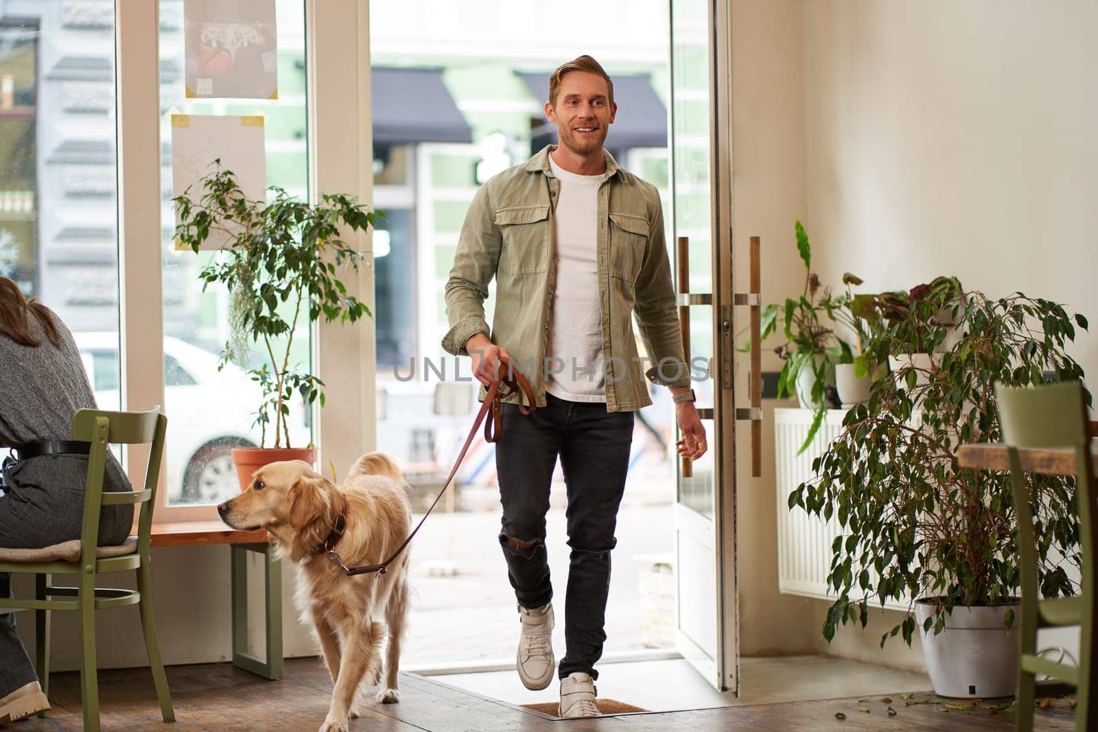 Portrait of handsome young man walks into the cafe with his dog on a leash, enters pet-friendly coffee shop, opens the door.