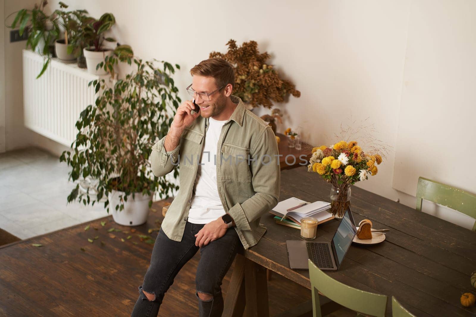 Portrait of handsome man in office, manager working in office, answering a phone call, talking to client over the telephone, sitting on table with laptop.