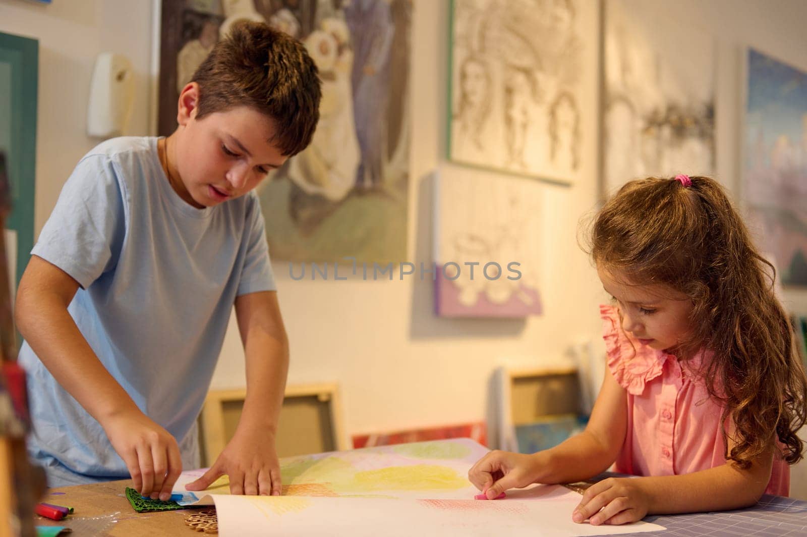 Kids drawing while learning art in the creative school. Fine art class with beautiful artworks displayed for sale in the art gallery