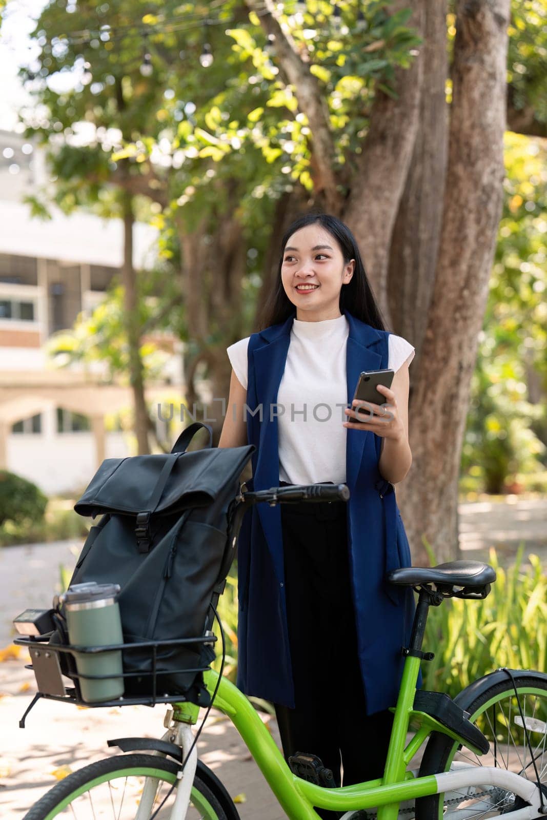 Asian businesswoman with bicycle using smartphone and outside the office building. Woman commuting on bike go to work. Eco friendly vehicle, sustainable lifestyle concept by nateemee