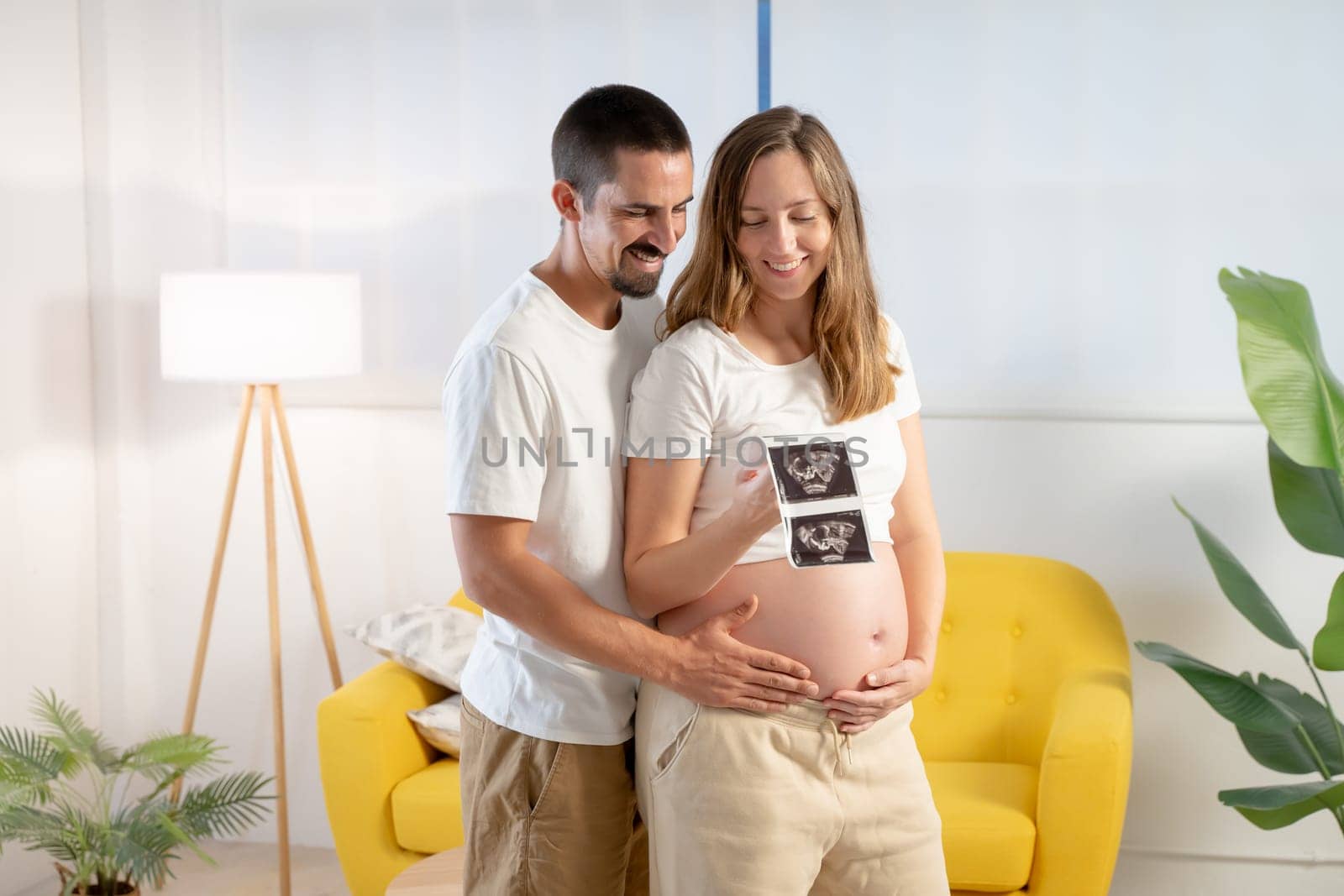 Pregnancy couple hugging looking picture of ultrasound, smiling happily touching belly. High quality photo