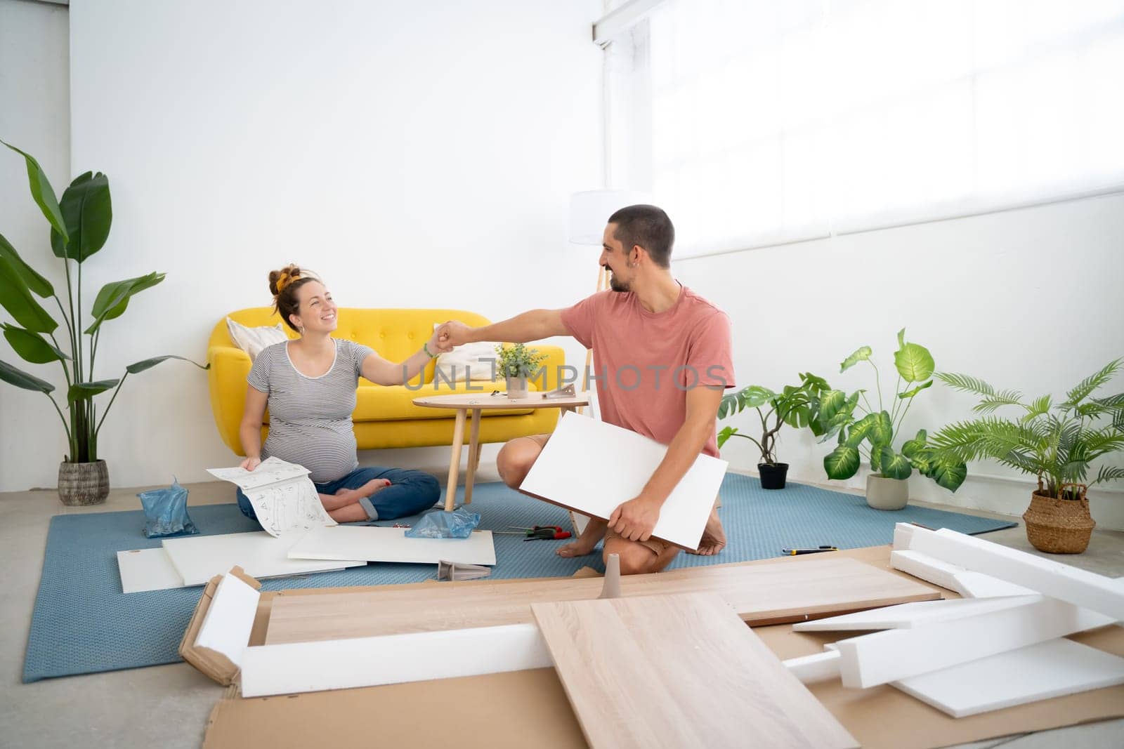pregnant couple happily holding hands while assembling furniture in the new house. High quality photo
