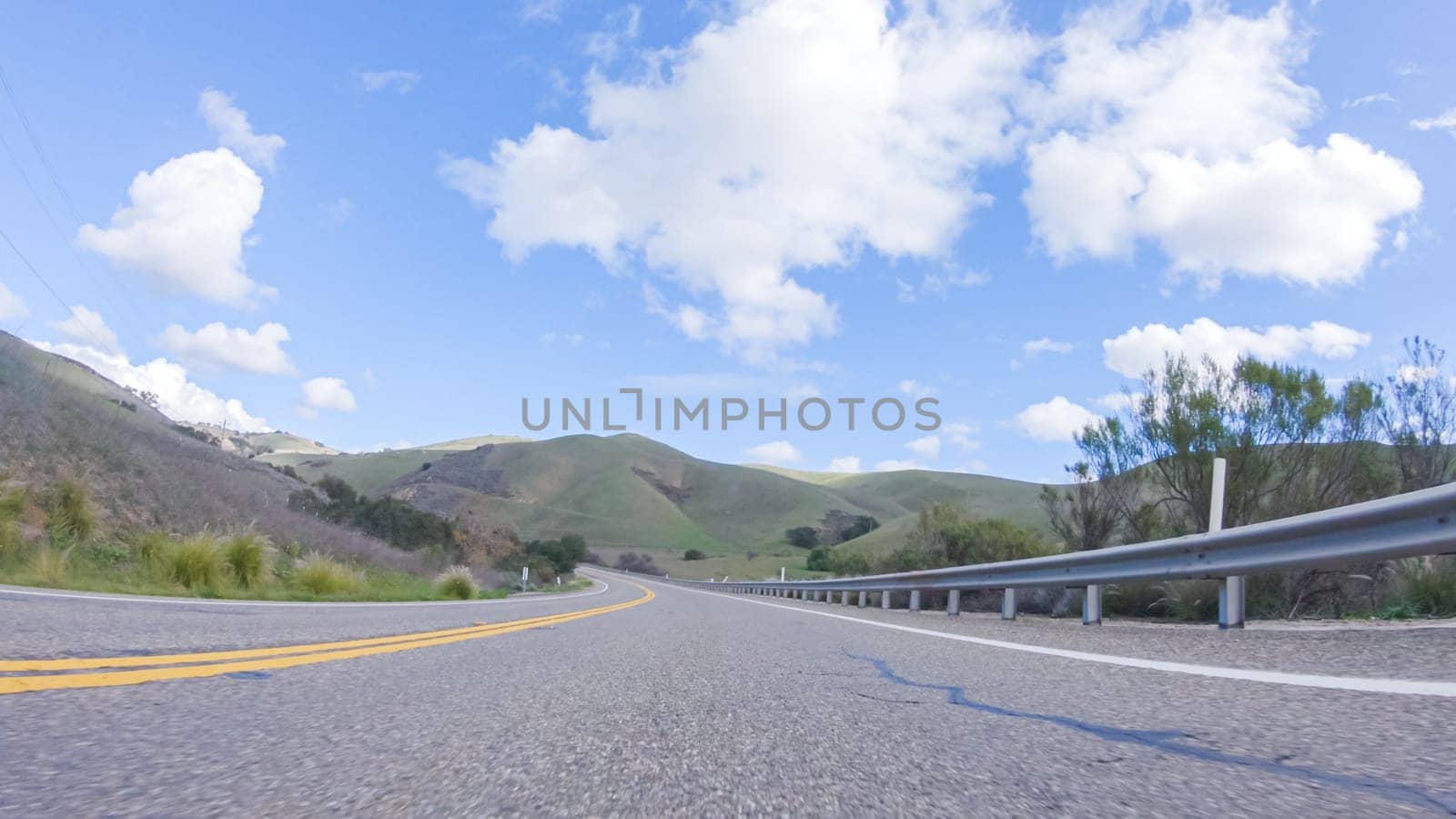 On a clear winter day, a car smoothly travels along Highway 101 near Santa Maria, California, under a brilliant blue sky, surrounded by a blend of greenery and golden hues.