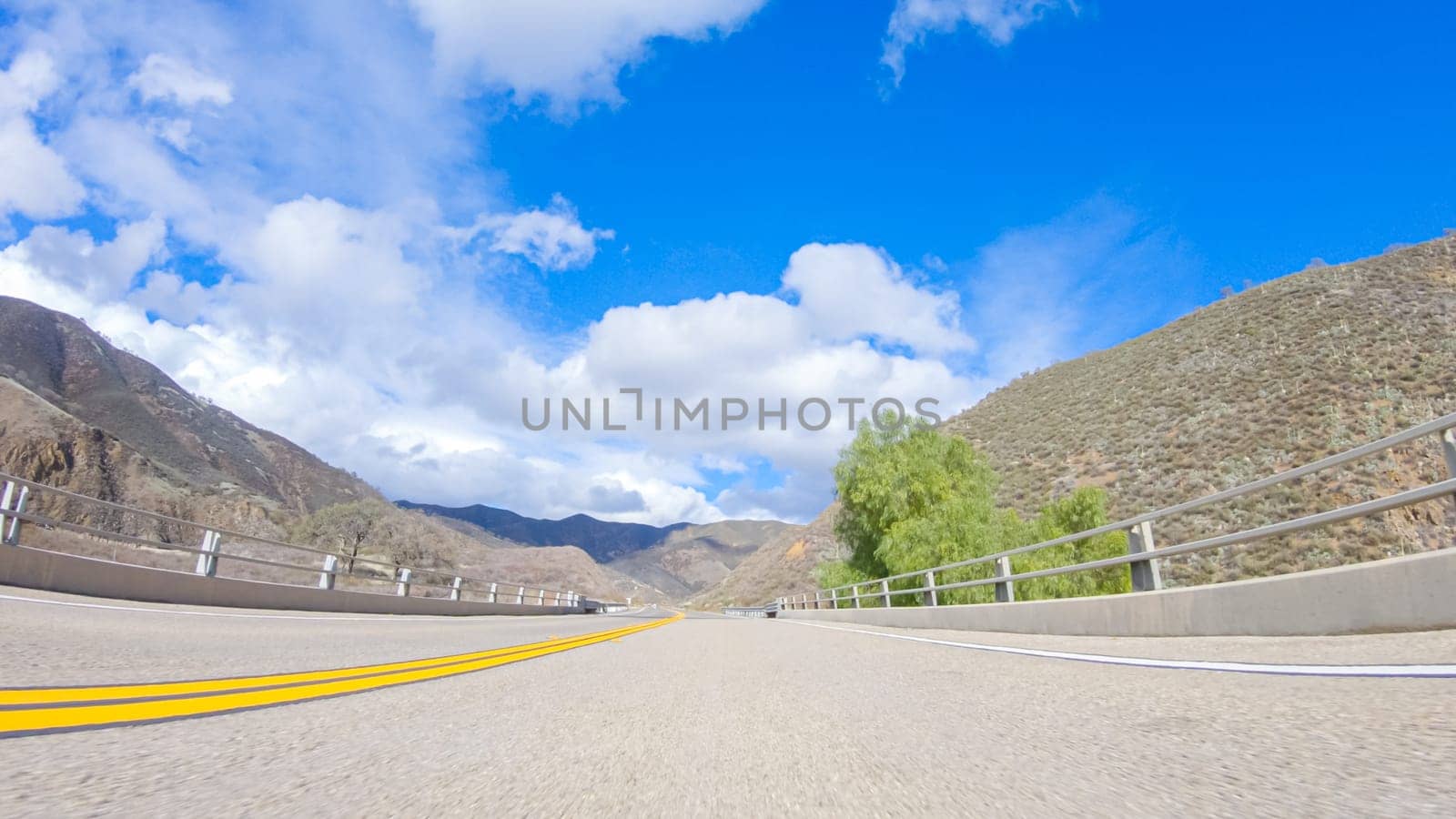 Vehicle is cruising along the Cuyama Highway under the bright sun. The surrounding landscape is illuminated by the radiant sunshine, creating a picturesque and inviting scene as the car travels through this captivating area.