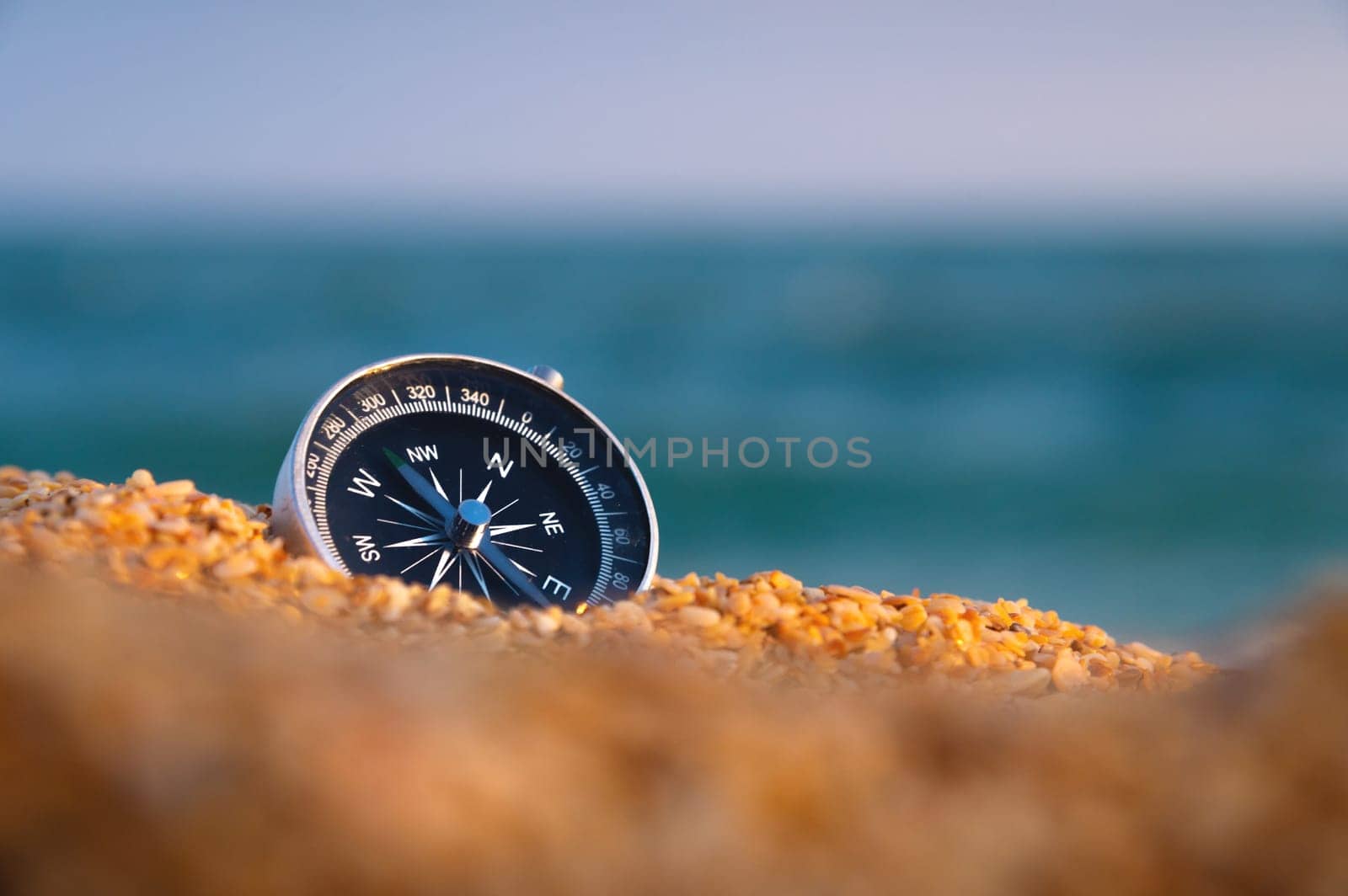 Conceptual photo of a compass in coarse sand against the background of the sea and sky, close-up, without people by yanik88