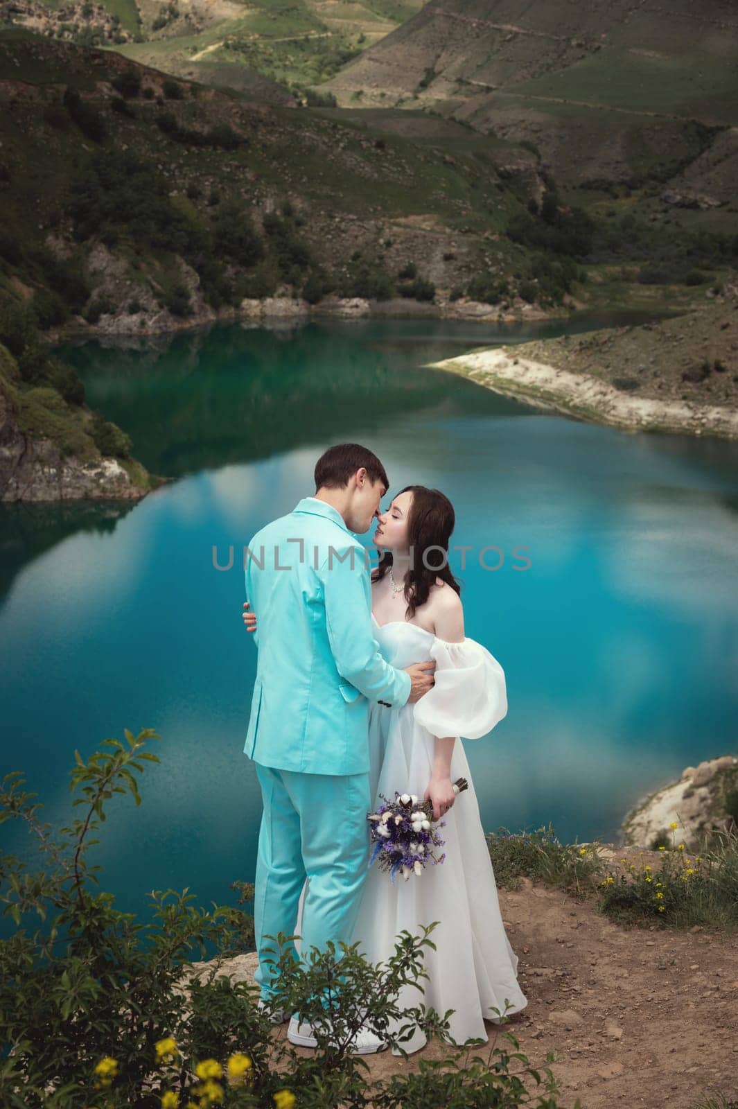 beautiful wedding couple hugs tenderly against the backdrop of a mountain river and lake, the bride's long white dress by yanik88