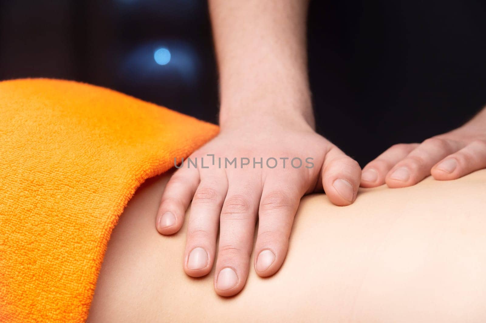 Close-up Side view in shallow depth of field. Massage of the lower back by a male masseur. Volumetric light. Live photography by yanik88