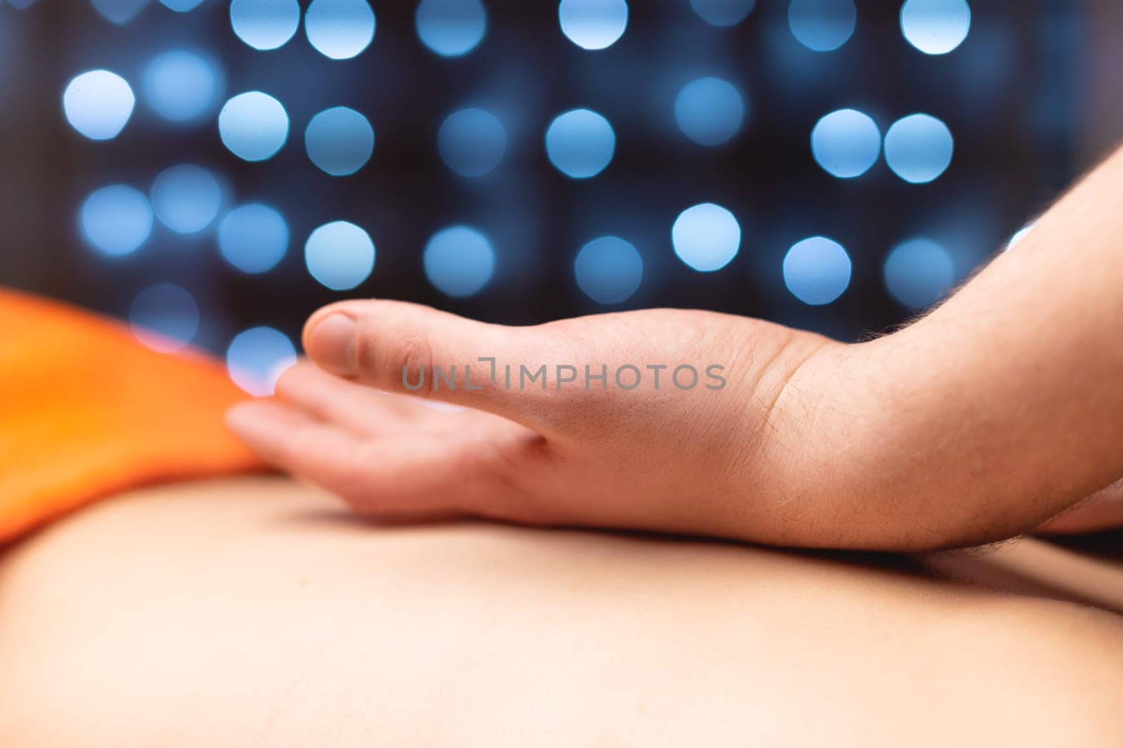 Close-up Side view in shallow depth of field. Massage of the lower back by a male masseur. Volumetric light. Live photography.