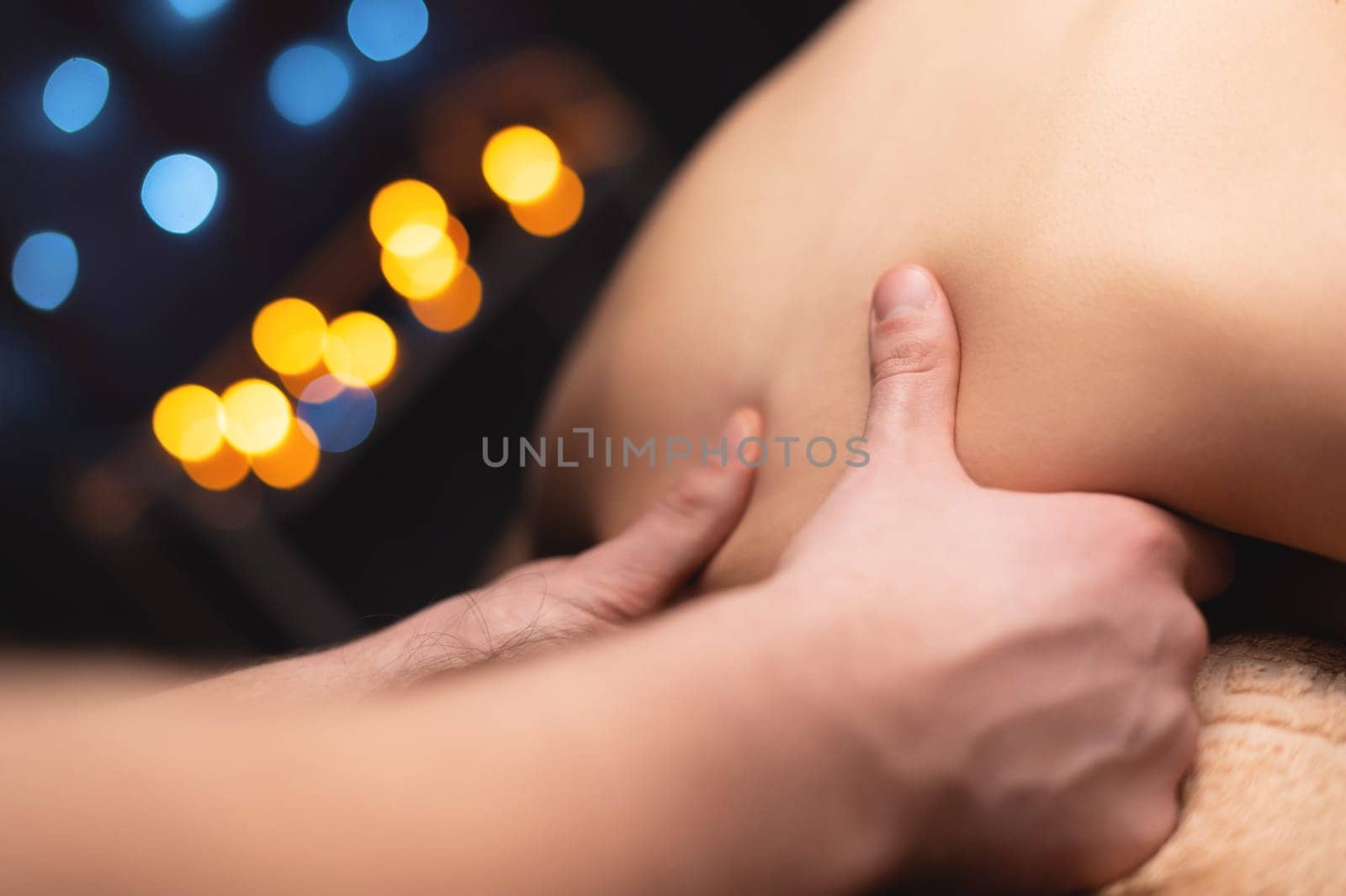 Close-up of a woman's neck and trapezium being massaged by a male masseur in shallow depth of field.
