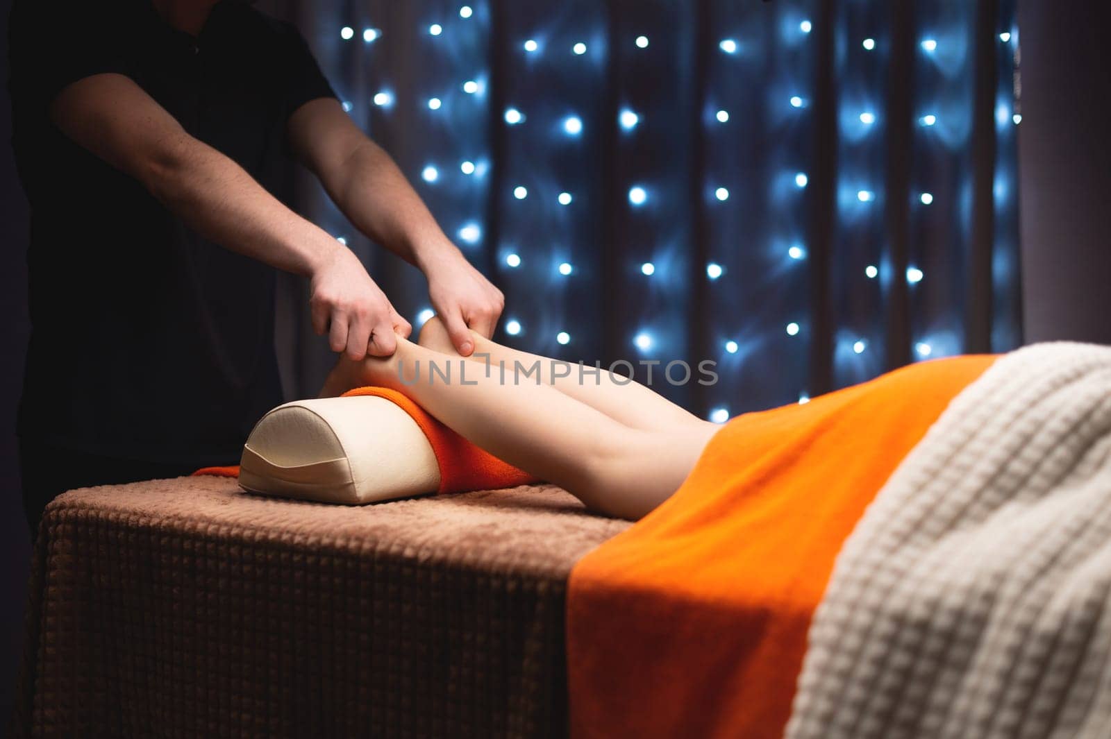 Close-up in shallow depth of field of a male masseur's hands massaging the Achilles tendon of a female leg. Professional massage in a professional room.