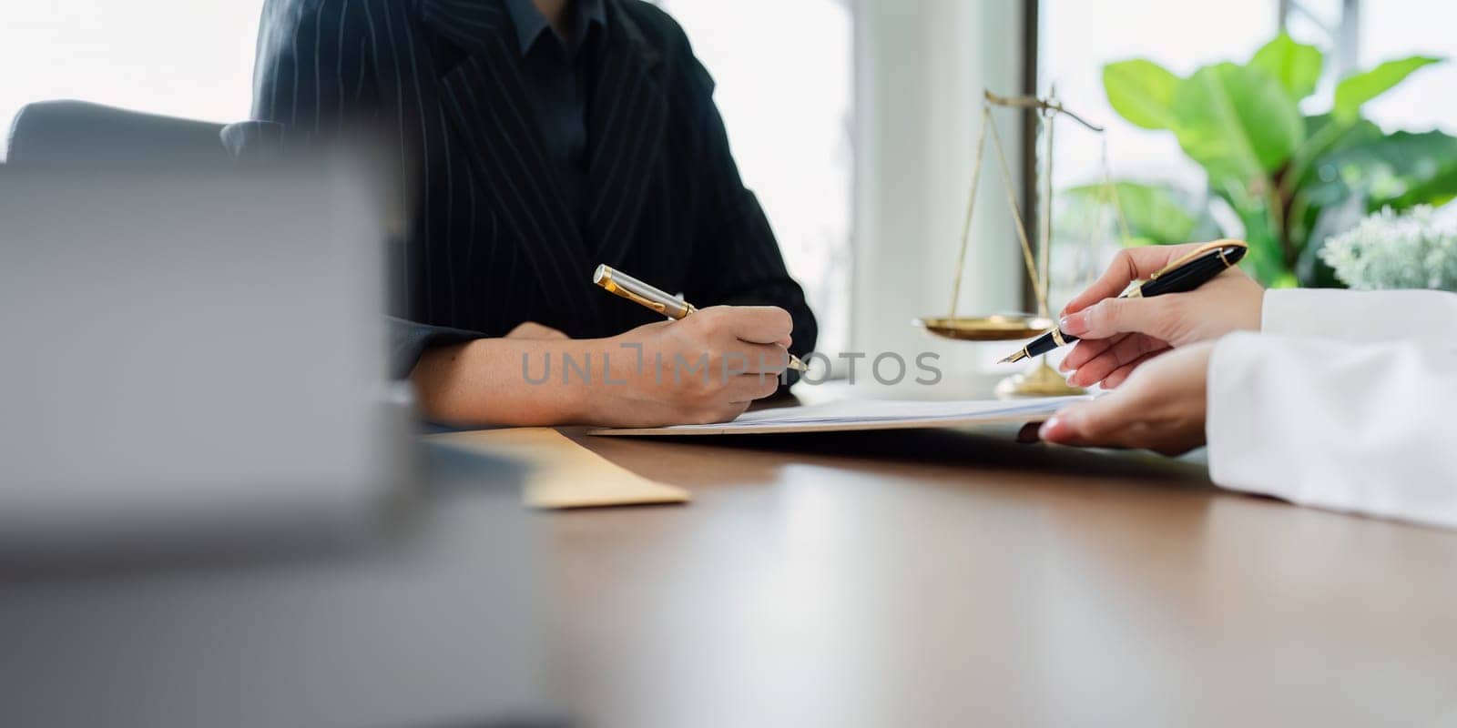 Two people are sitting at a table with pens and papers in front of them. They are discussing something important