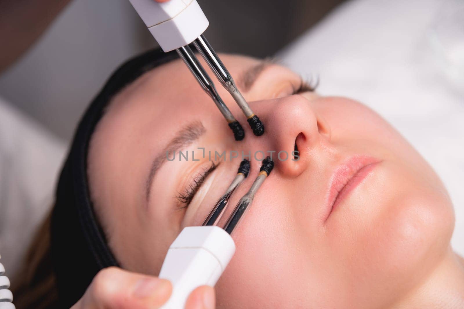 Close-up portrait of a beautiful woman with closed eyes and a skin rejuvenation machine. Salon procedures. Microcurrent therapy.