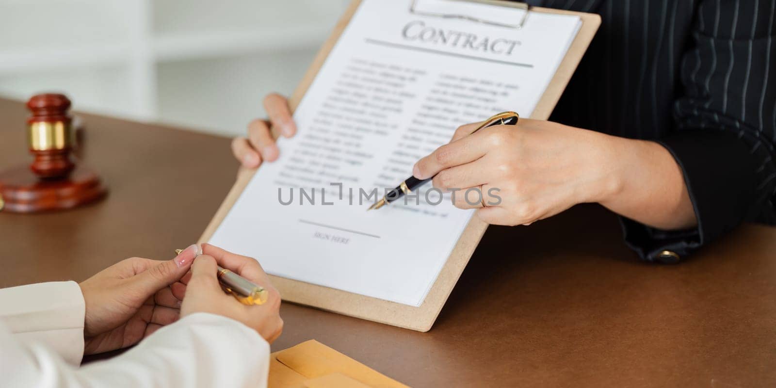 Two people are sitting at a table with pens and papers in front of them. They are discussing something important