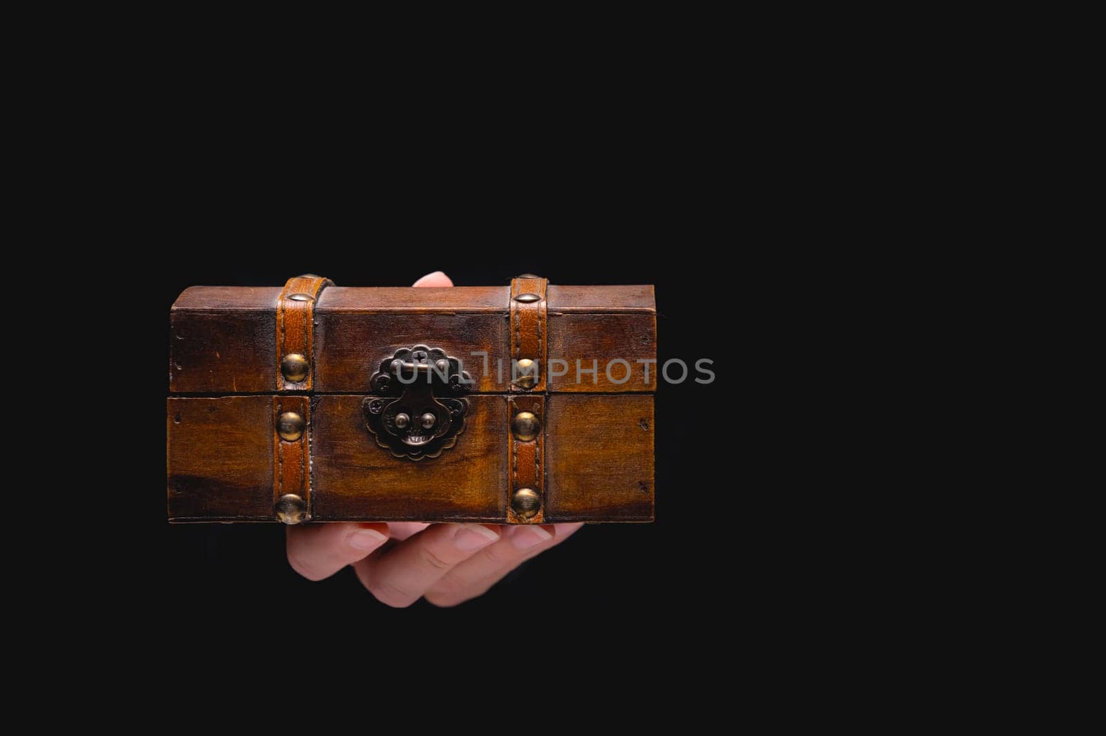 An old wooden box chest on a young female hand on a black background. Nice gift concept in gothic vintage style.