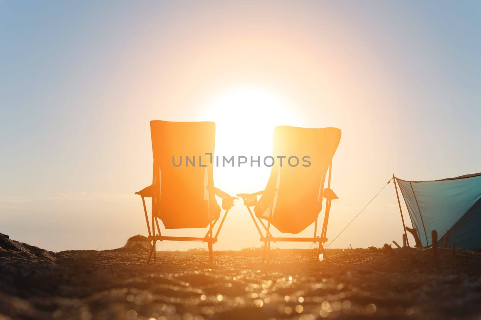 Two folding camping chairs against the backdrop of the setting sun. Camping tourism. Nobody.